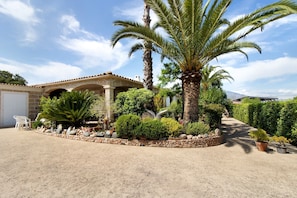 A house with a stone facade, a covered patio, and a well-maintained garden with various plants and a palm tree. - Sea and Canopy Rooms: Mountain View, Shared Terrace and Garden (SARROLA CARCOPINO)