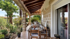 An outdoor patio with a wooden table and chairs, surrounded by potted plants and a stone wall. - Sea and Canopy Rooms: Mountain View, Shared Terrace and Garden (SARROLA CARCOPINO)