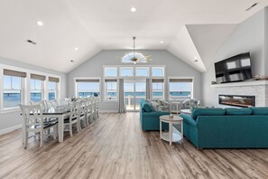A spacious living area with a large dining table, teal sofas, and a fireplace. - Livin' The Dream: Soundfront | Pool | Hot Tub (Rodanthe)