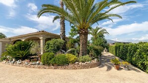 A well-maintained garden with palm trees, a stone pathway, and a building with a tiled roof. - Bed and Breakfast 'Gautama' with Mountain View, Shared Terrace and Shared Garden (SARROLA CARCOPINO)