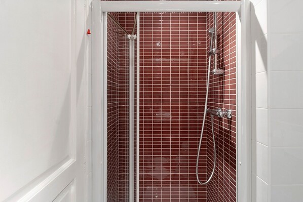 A shower with a white door and red-tiled walls.
