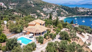 Una villa mediterránea con piscina, rodeada de exuberante vegetación y una vista panorámica al mar.