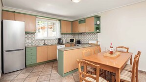 Cocina compacta con refrigerador, microondas y cafetera. Cuenta con una mesa de comedor con sillas y un estante pequeño encima.