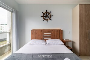 Een hotelkamer met een bed, een houten hoofdeinde, een aan de muur bevestigd decoratieve stuurrad en een klein nachtkastje, plus een kledingkast.