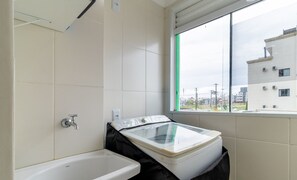 Een badkamer met een bad, een raam met uitzicht op gebouwen en een witte betegelde muur.
