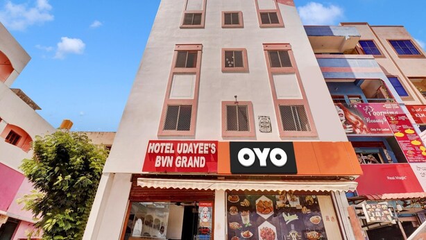Egy többemeletes szálloda, amelyen feltűnő tábla hirdeti a „Hotel Udayee's Bvn Grand” és az „Oyo” márkanevet.