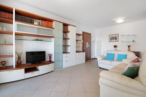 Una sala de estar con televisor, sofá y estanterías abiertas con libros.
