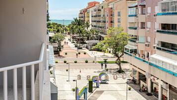 A multi-story building with balconies, a pedestrian area with trees, and a view of the sea.
