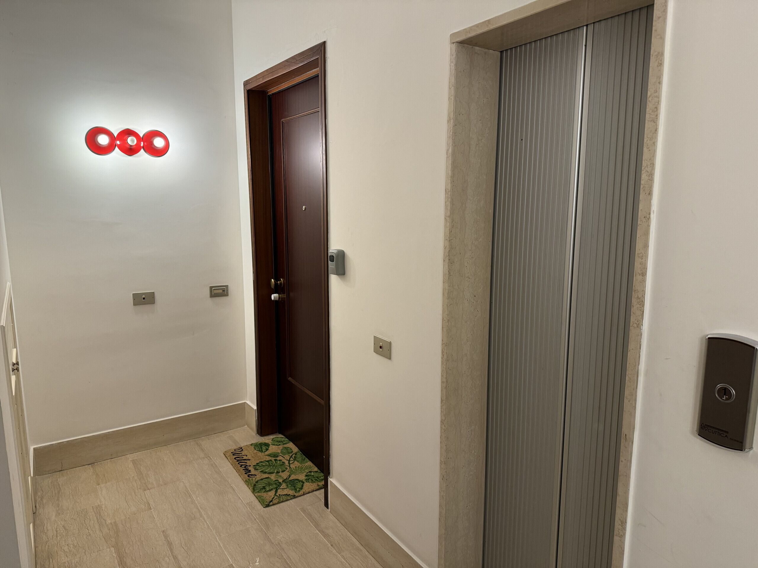 A hallway with a wooden door, a doormat, and a wall-mounted intercom.