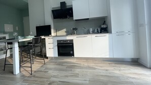 A modern kitchen with white cabinets, a built-in oven, and a dining area with a table and chairs.