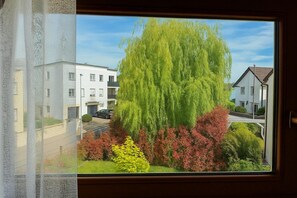 A window with a view of a residential area, including a large tree and buildings. - Apartment 'Blaues Apartment' with Two South-Facing Balconies, Shared Garden and Wi-Fi (Bad Krozingen)