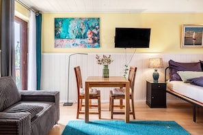 Une pièce comprenant un lit, un canapé, une table à manger avec des chaises, un téléviseur fixé au mur et un tableau au-dessus de la table.