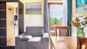 Una habitación con sofá, una mesa de comedor, una silla, un armario de madera, un cuadro y vistas por una ventana.
