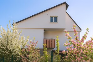 A modern two-story house with a flat roof, a small window, and a balcony with brown shutters. - Apartment 'Blaues Apartment' with Two South-Facing Balconies, Shared Garden and Wi-Fi (Bad Krozingen)