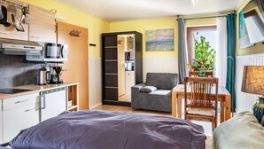 Habitación pequeña con cama, kitchenette, zona de comedor y vista por una puerta abierta.