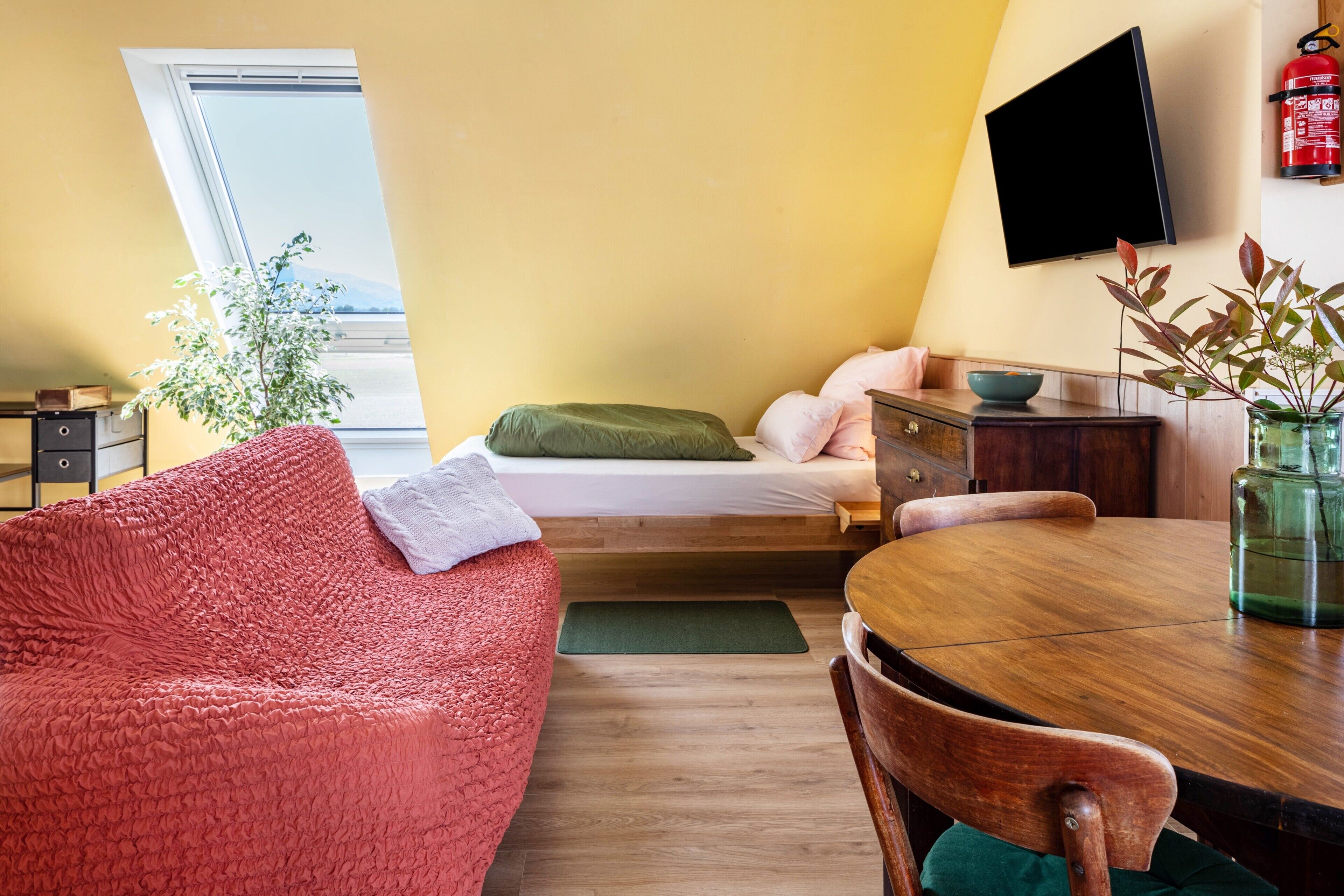 Una habitación compacta con cama, sofá, mesa de comedor y televisor montado en la pared.