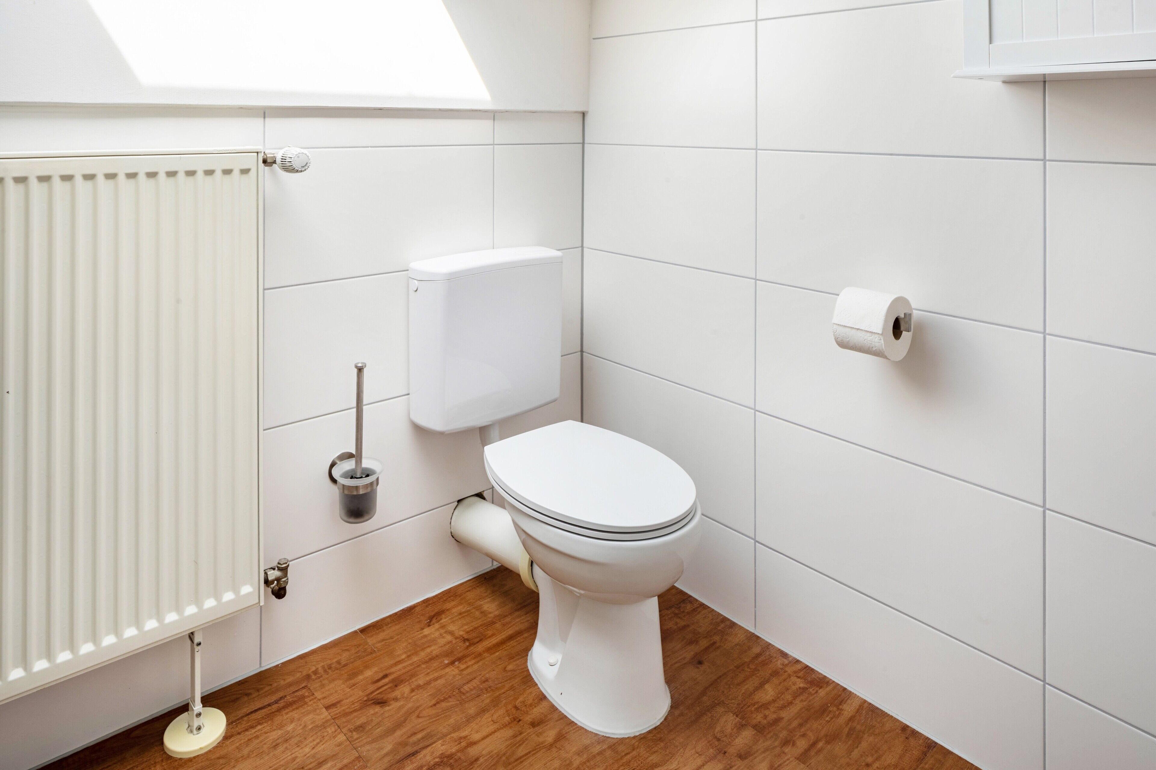 Een badkamer met een toilet, een radiator en een rol toiletpapier aan de wand.