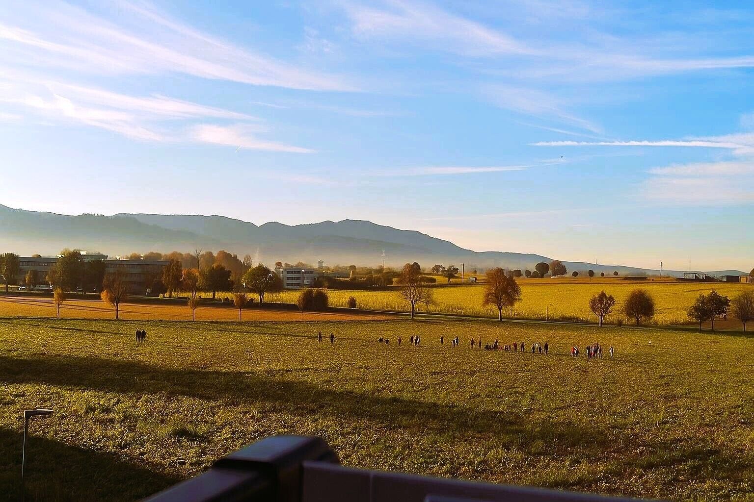 A rural landscape with fields, trees, and distant mountains under a clear sky.