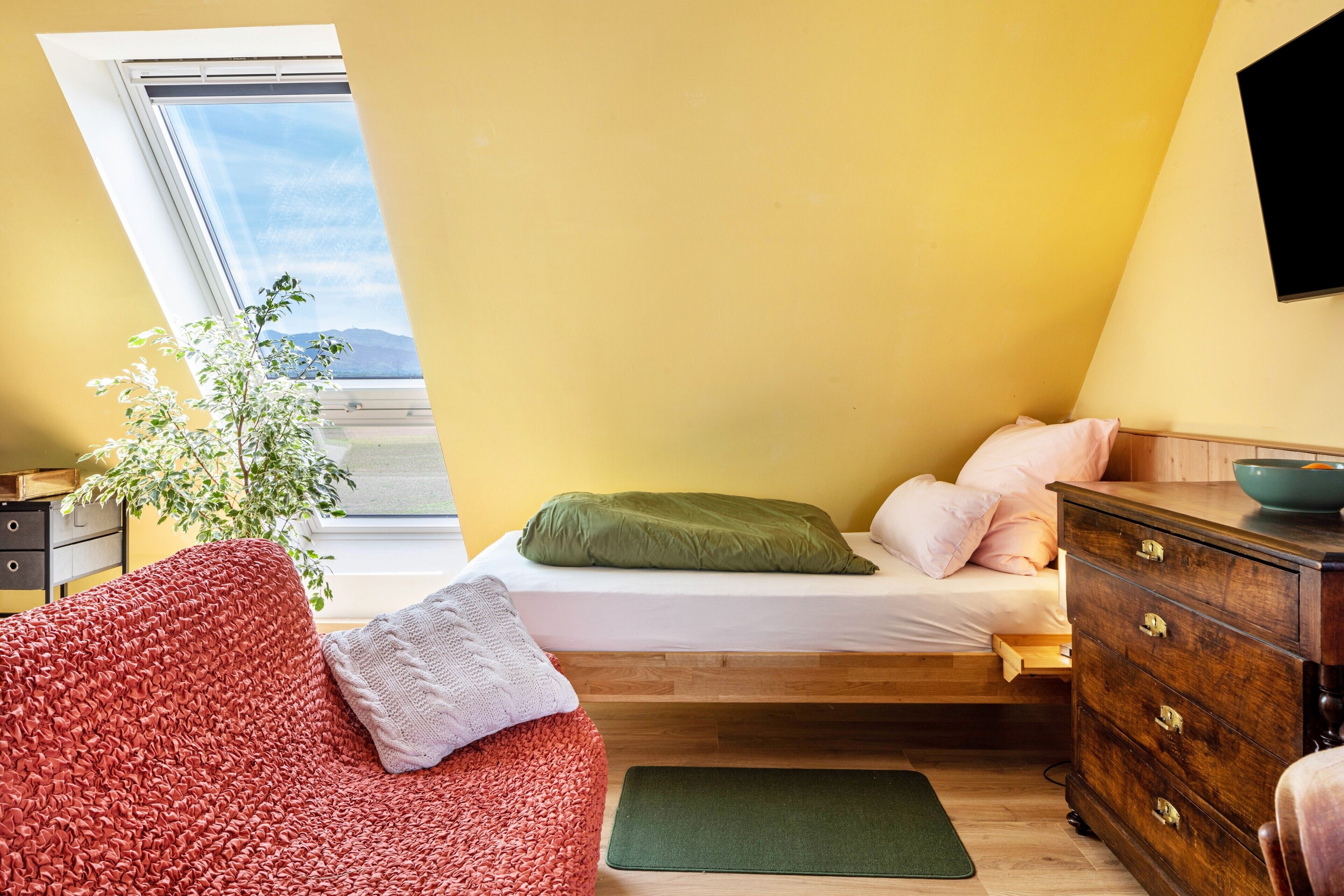 Ein Schlafzimmer mit Bett, einem Schminktisch, einem roten Sofa, einer grünen Matte und einem Fenster mit Aussicht.