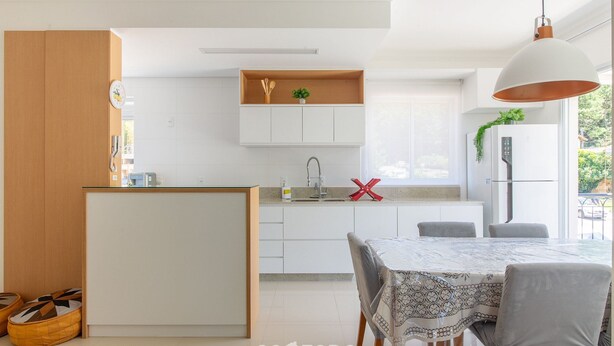Uma cozinha moderna com armários brancos, uma ilha central e uma área de jantar com mesa e cadeiras.