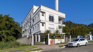 Edifício residencial de vários andares com design arquitetônico moderno, com varandas e entrada protegida por portão.