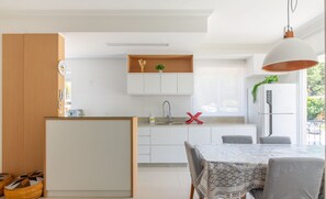 A modern kitchen with white cabinetry, a central island, and a dining area with a table and chairs. - Beautiful apt With Barbecue in Floripa Ibe104 (Florianópolis)