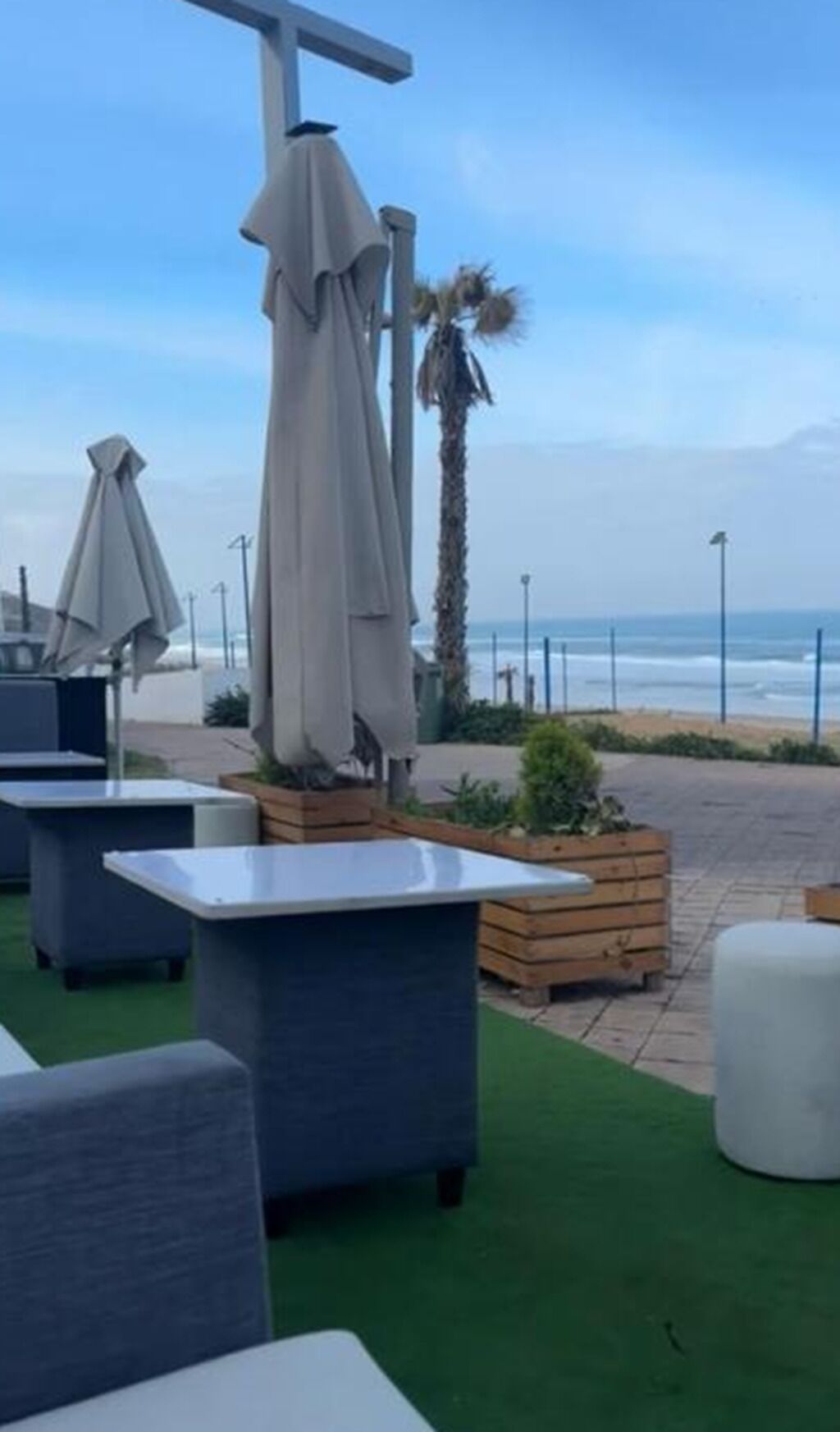 Espace extérieur aménagé avec des tables et des parasols, un jardinier en bois et vue sur la plage.