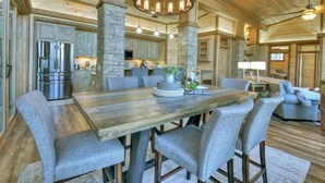 Une cuisine spacieuse avec une grande table en bois, des chaises à revêtement gris et un lustre moderne.