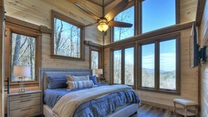 Une chambre à coucher avec un grand lit, de nombreuses fenêtres et un ventilateur de plafond.