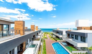 Hotel moderno com piscina no terraço, vista para o mar e um jardim bem cuidado.