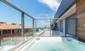 A rooftop pool with glass railings, a view of the sea, and a modern building with wooden accents.