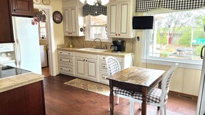A kitchen with wooden cabinets, a dining table with checkered chairs, a ceiling fan, and a window with a view of the backyard.