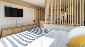 Un dormitorio con cama, televisor montado en la pared y un panel de madera con diseño tejido.