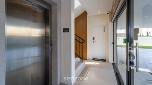 Una entrada de edificio moderna con un ascensor metálico, una puerta de madera y una puerta de cristal que da al exterior.