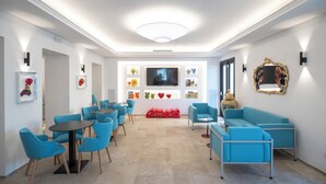 A modern lounge area with blue furniture, a large TV screen, and decorative items on the walls. - Hotel Palazzo Antonietta (Castellabate)