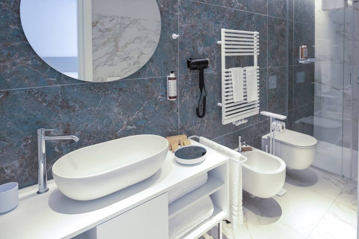 A modern bathroom with a large oval sink, a round mirror, a hairdryer, and a toilet.