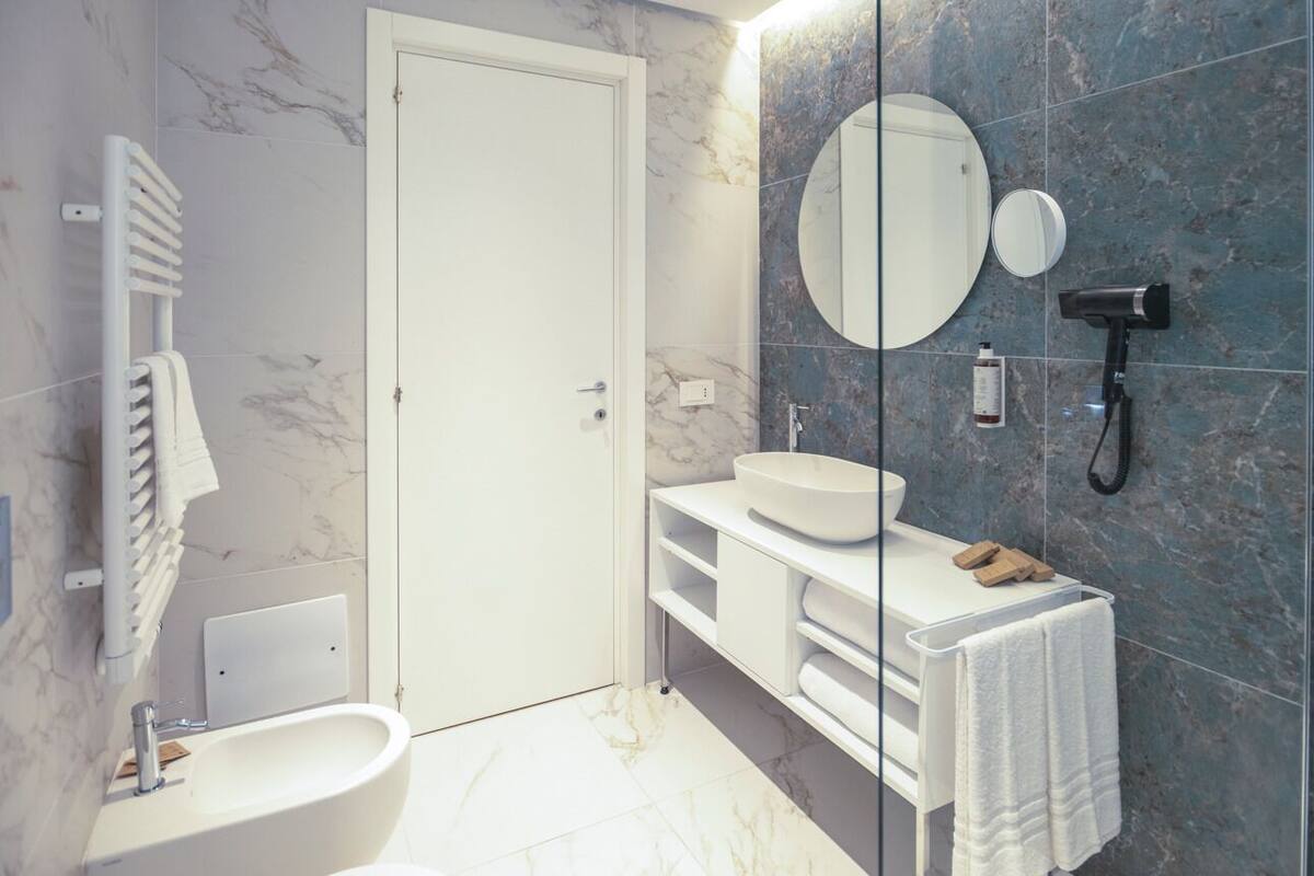 A modern bathroom with a white sink, a mirror, a handheld showerhead, and a towel rack.