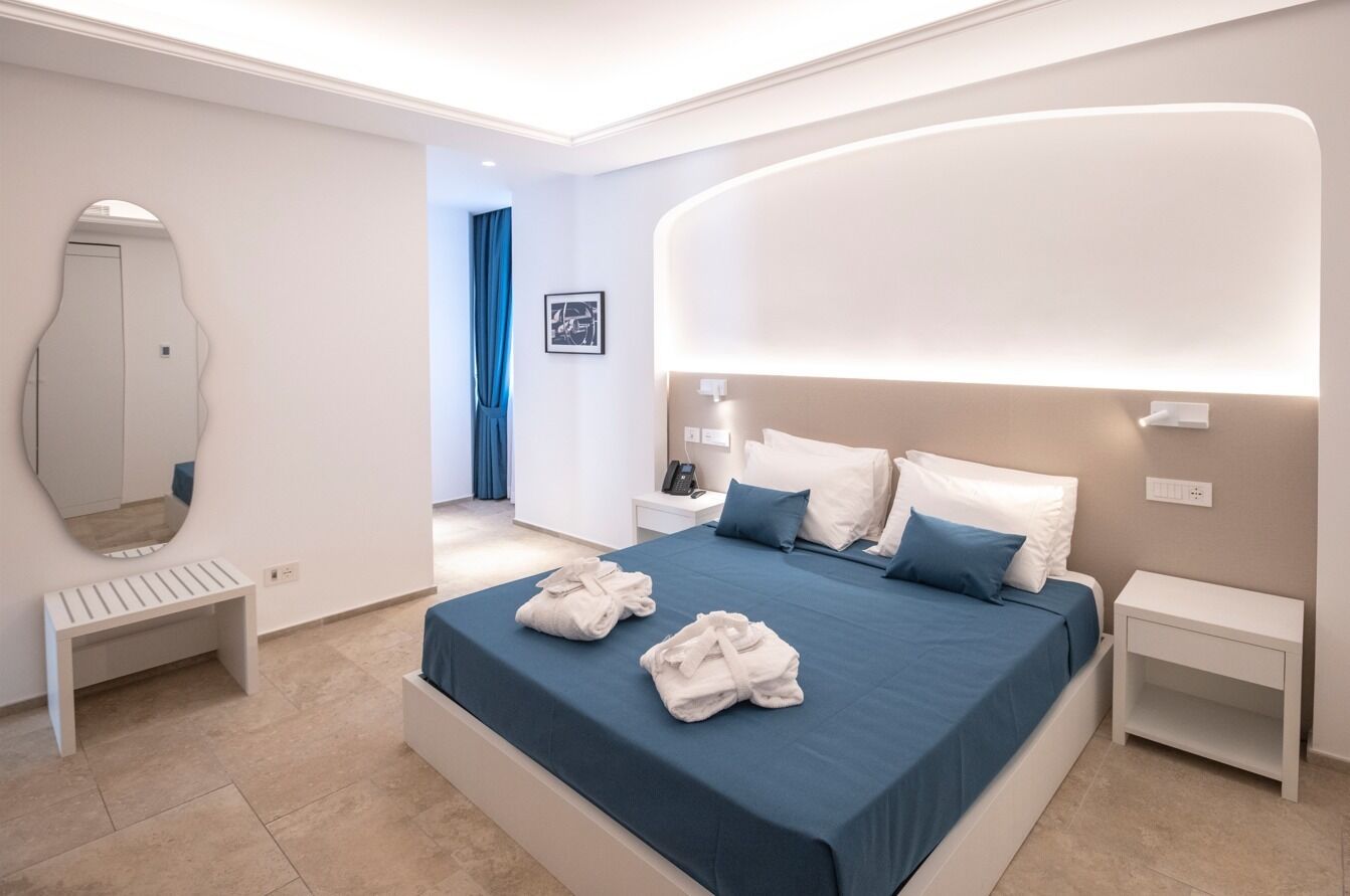 A modern hotel room with a large bed, bedside tables, a bench, and a mirror.