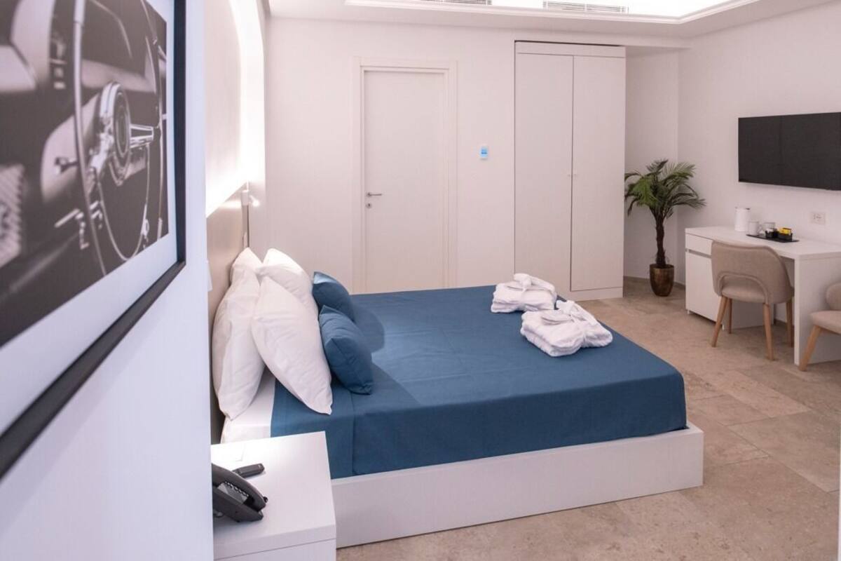 A modern hotel room with a bed, a desk, a chair, a TV, and a plant.