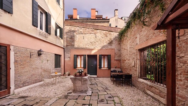 A courtyard with stone paving, a central table with chairs, and a door leading to a building with brick walls and shutters. - Huge design apartment in the center of Venice, with private courtyard (Venezia)