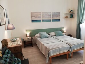 A double bed with striped bedding, two bedside tables with lamps, a small wooden nightstand with a lamp, a framed picture on the wall, and a shelf with books and a vase. - Family apartment in the center of Florence (Firenze)