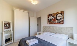 A bedroom with a bed, a wardrobe, a mirror, a bedside table, and a painting on the wall.