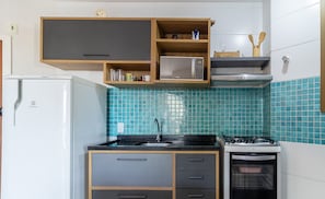 A compact kitchen with a refrigerator, stove, microwave, and a sink.
