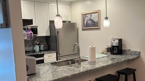 Une cuisine moderne dotée d’un comptoir en granit, d’appareils électroménagers en acier inoxydable et de tabourets de bar noirs.