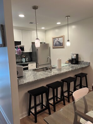 A modern kitchen with a marble countertop, stainless steel appliances, and black bar stools.