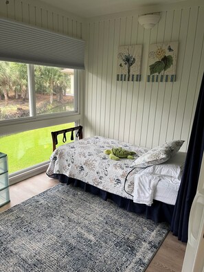 A bedroom with a bed, a window, a view of greenery, and wall art.