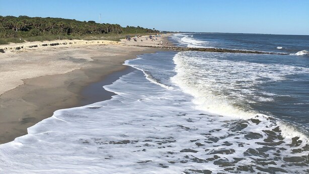 Une plage avec des vagues, un rivage sablonneux et un ciel dégagé.