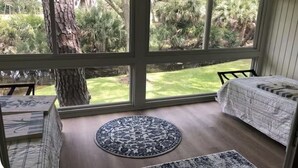 Une chambre avec une grande fenêtre, un tapis rond et un lit recouvert d’une couvre-lit à motifs.