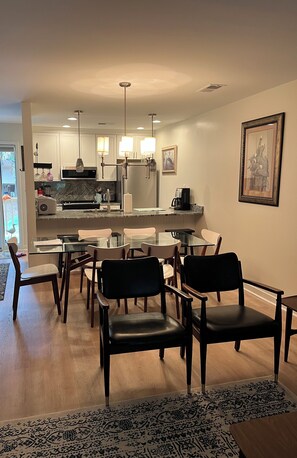 A modern kitchen with a dining area, featuring a glass table, chairs, and a patterned rug.