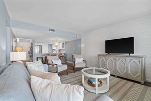 Una sala moderna con sofá, sillones, una mesa de centro y un televisor sobre un mueble.